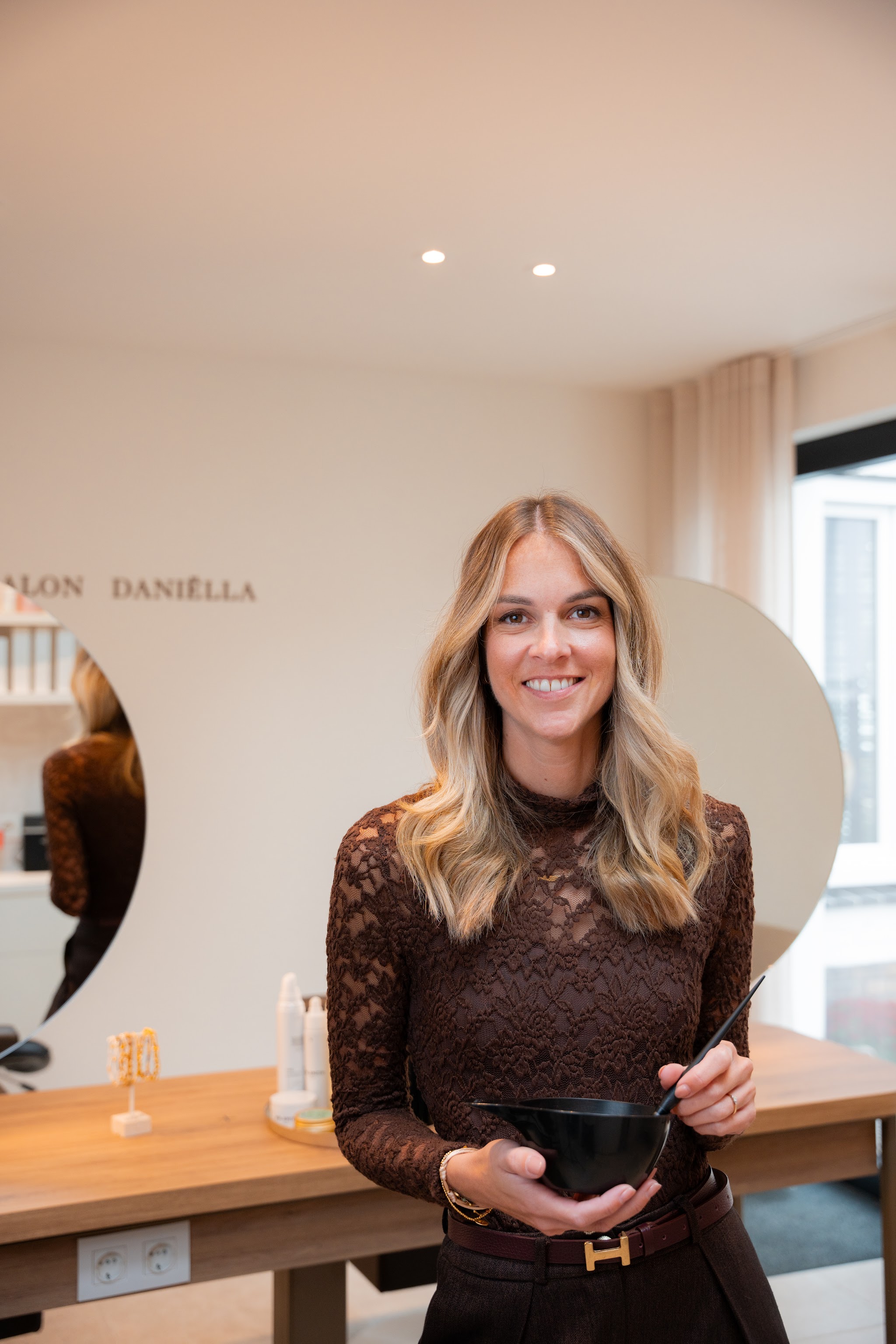 Daniëlla in haar salon met een kleurbakje, voor de letters van Kapsalon Daniëlla op de wand