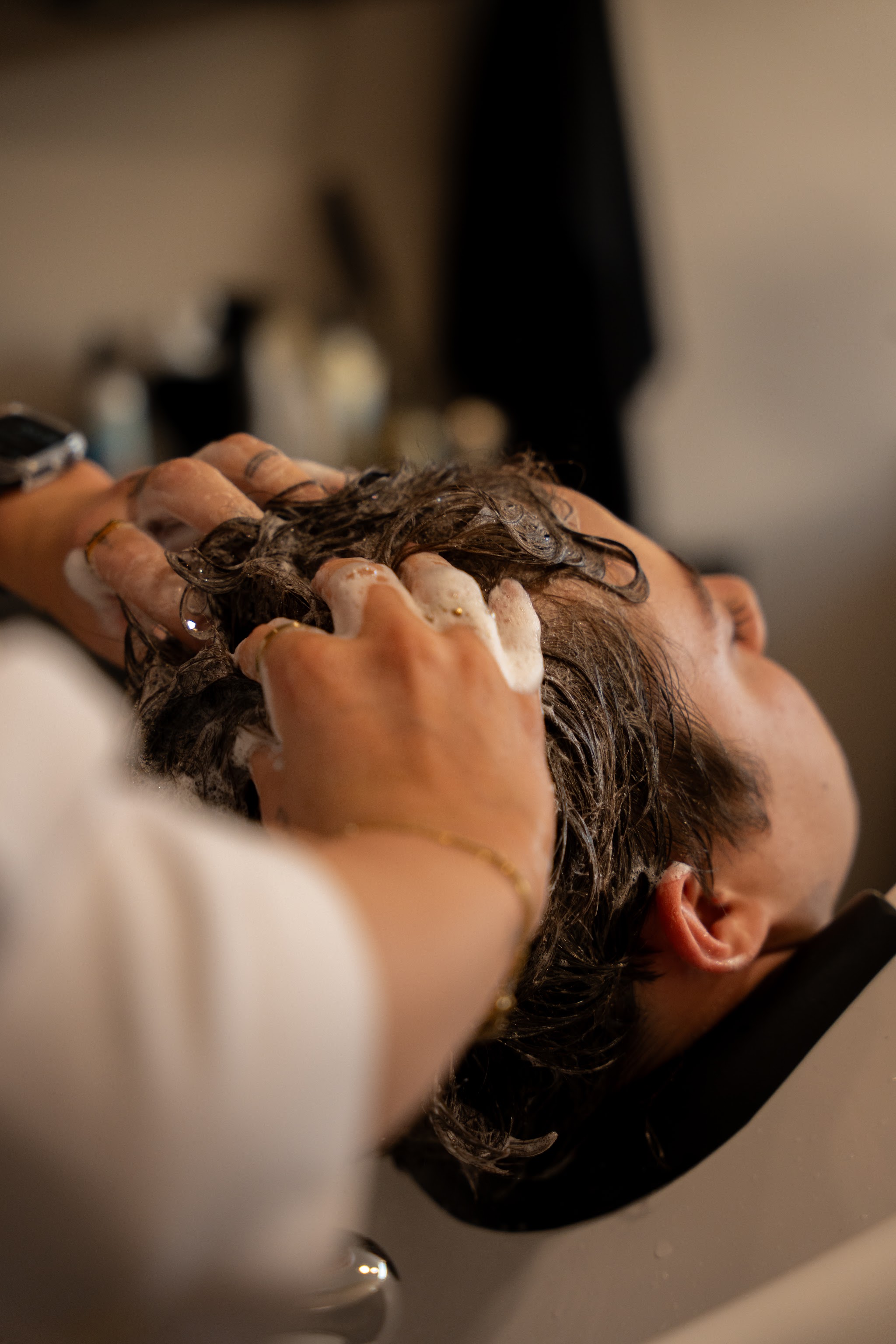 Een klant ontspant bij de wasbak terwijl haar haar gewassen wordt, met een hoofdmassage