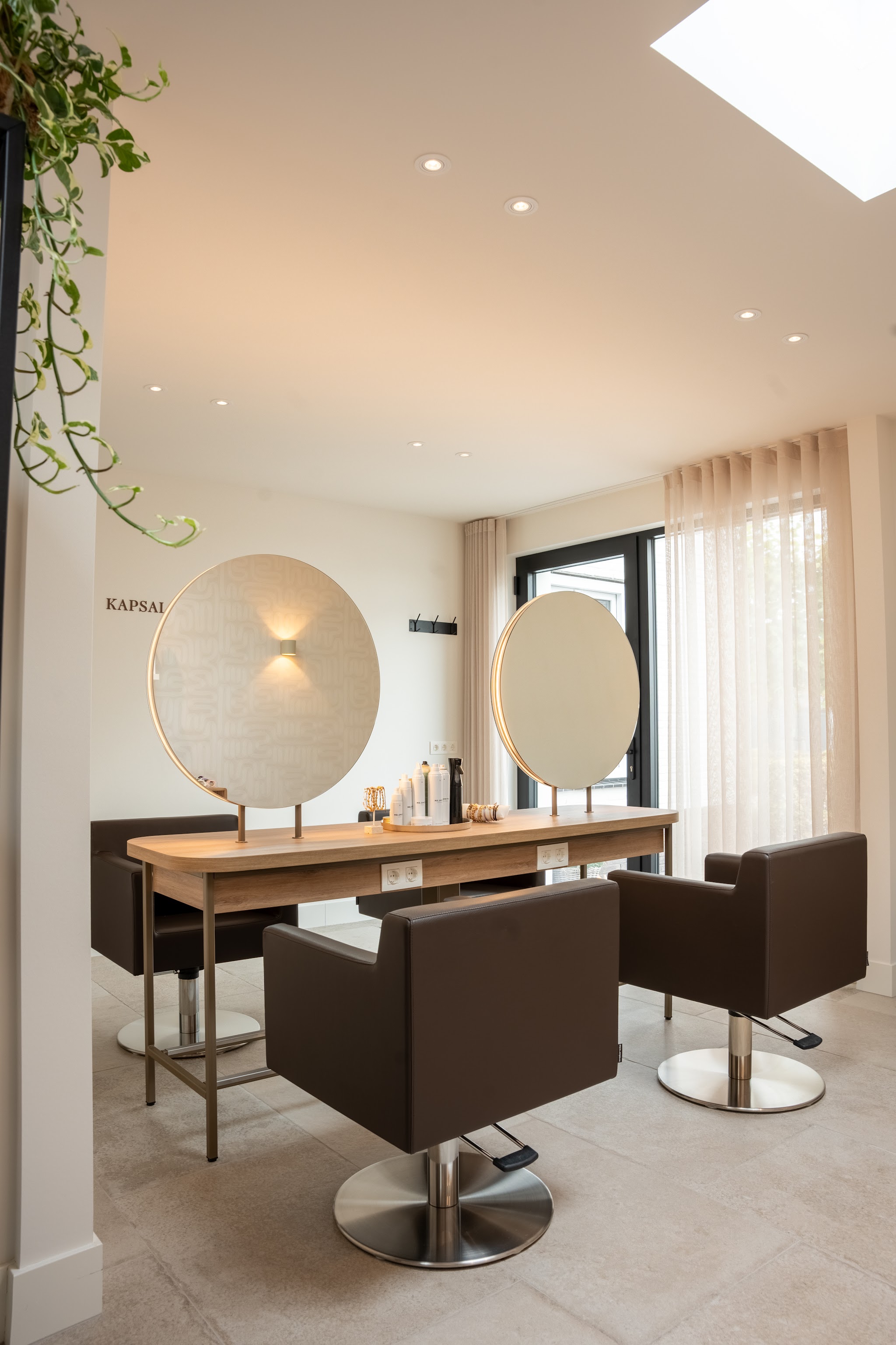 De salon met twee ronde spiegels, een eiken werktafel en bruine kappersstoelen