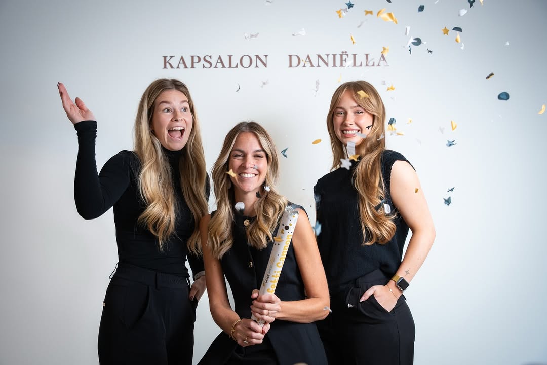 Het team van Kapsalon Daniëlla onder de confetti, voor de letters op de wand